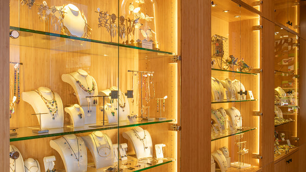 Rich wooden jewelry cases with glass fronts lit from inside featuring an assortment of necklaces, earrings, and rings.
