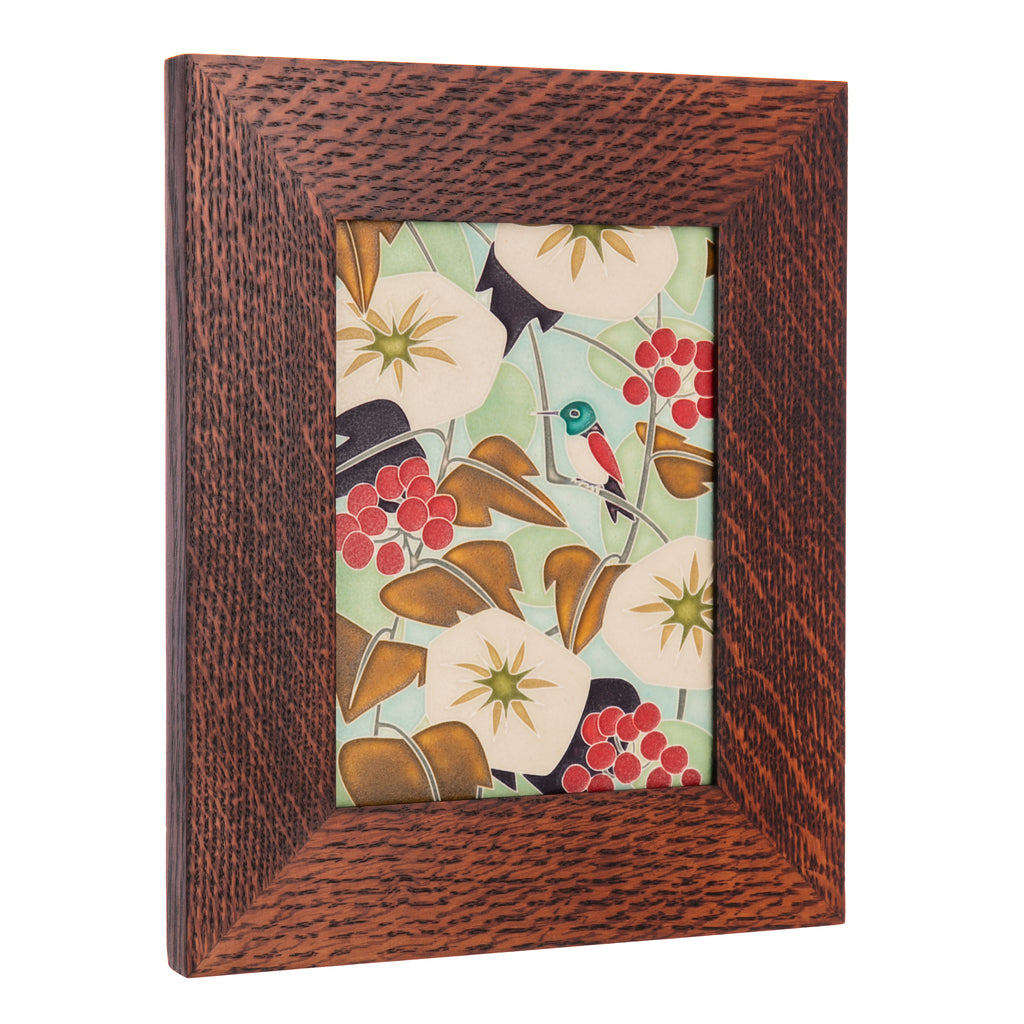 This high-quality framed tile by Motawi Tileworks features a design by Cary Phillips. It shows a hummingbird perched on a branch, surrounded by flowers, berries, and leaves. This Arts and Crafts style framed tile is the perfect addition to any home. Handmade. Frame - quartersawn oak. Framed tile size: 9" x 11".