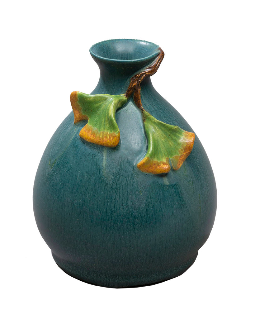 Two delicate ginkgo leaves flutter at the neck of this small, hand glazed teal colored bottle form. Thrown, sculpted & glazed by hand Approximately 4.25″H x 3.25″W Traditional earthenware art pottery is porous, glass liner recommended for use with water.