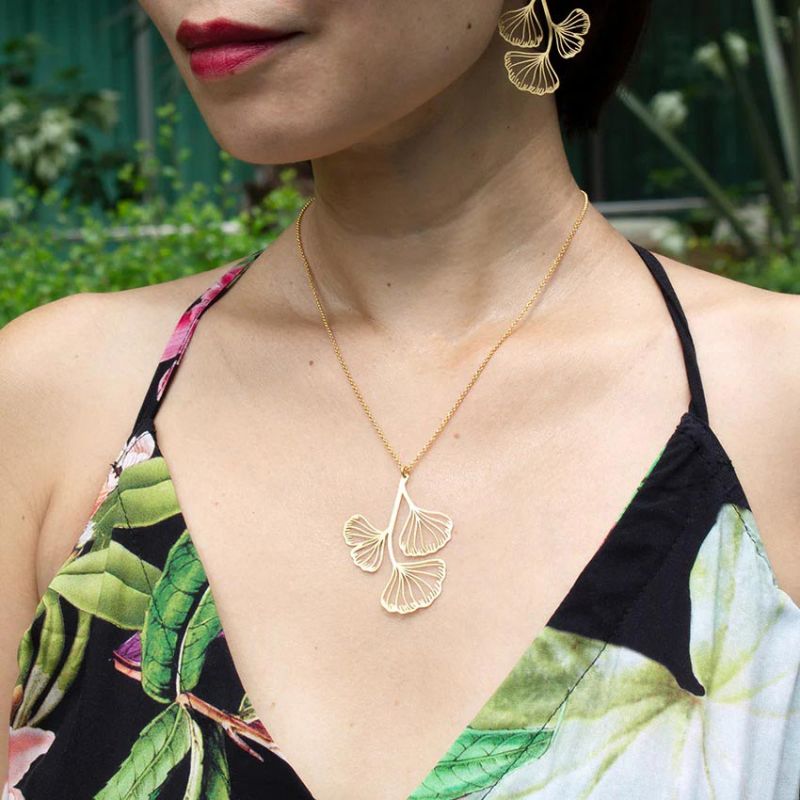 The fan-shaped ginkgo leaves are celebrated in this gold-plated necklace. This ginkgo necklace would look stunning as an addition to any outfit. Pair with other gold jewelry or wear on its own. Dimensions: Pendant - Approx. 1.5" x 2", Chain - Approx. 16"-21" Material: Gold-plated brass Nickel-free Made in Spain