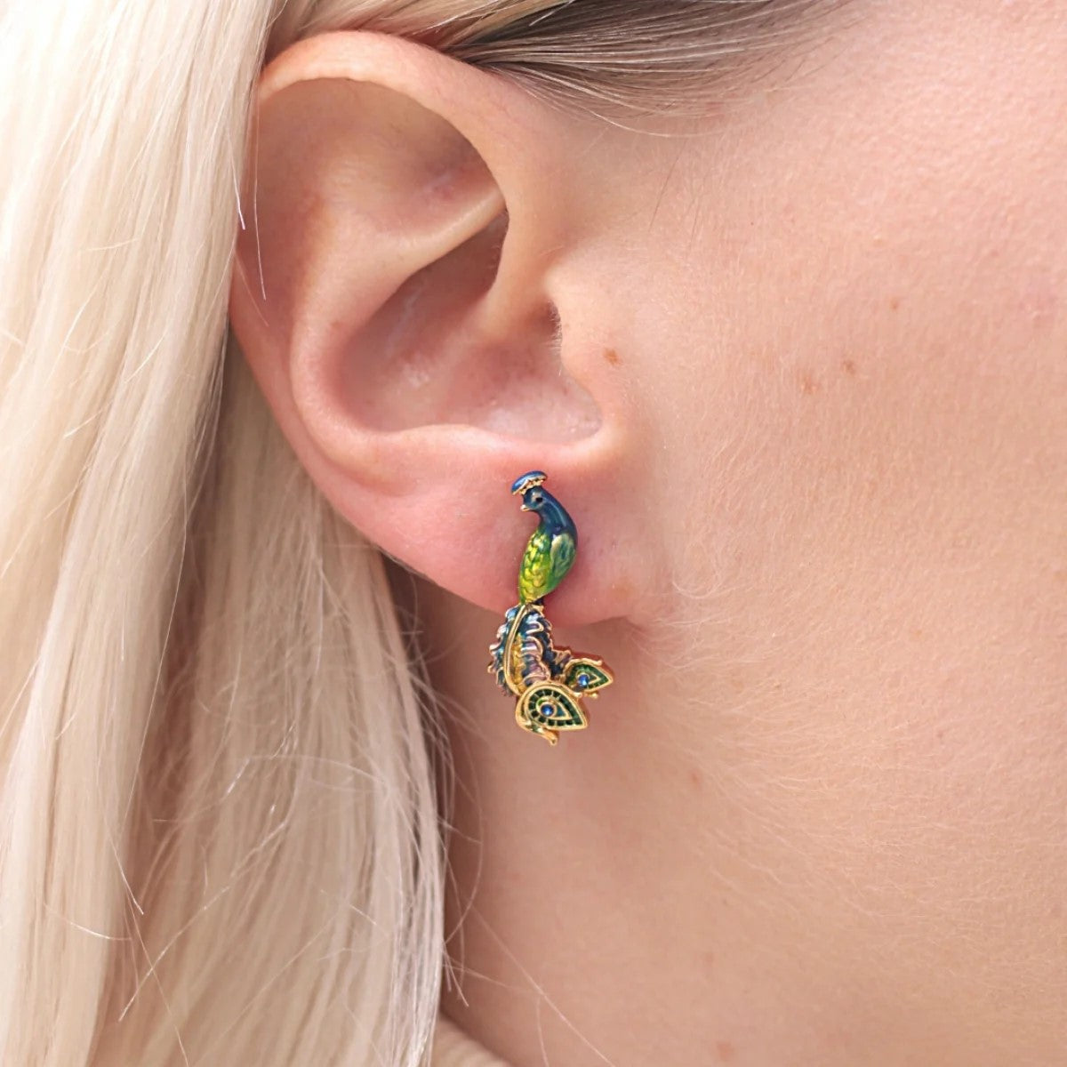 Peacocks are a symbol of strength and confidence in some cultures. Evoke that confidence with these gold-plated stud earrings featuring a hand-crafted enamel peacock. With crystal detail on the tail, these earrings will make a statement.  Dimensions: Approx. 0.4" x 1" Materials: Gold-plated Brass, Enamel Stud Post