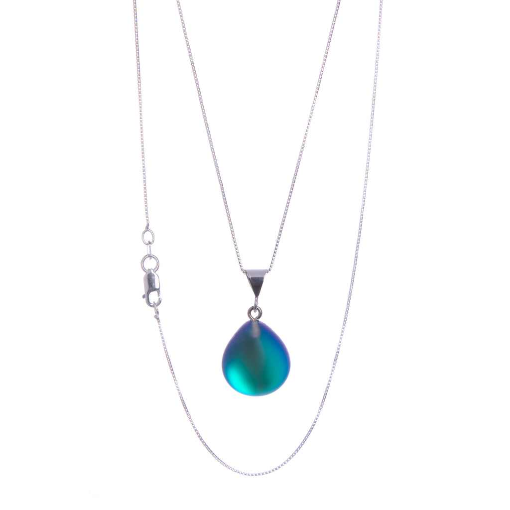 This pendant necklace features a simple, elegant teardrop shape crafted from frosted crystal layered with precious metals. The color changes from green to blue depending on the lighting and the wearer’s skin tone. Crystal and precious metals with a sterling silver box chain. Chain length: 18". Pendant size: 1" x 0.56".