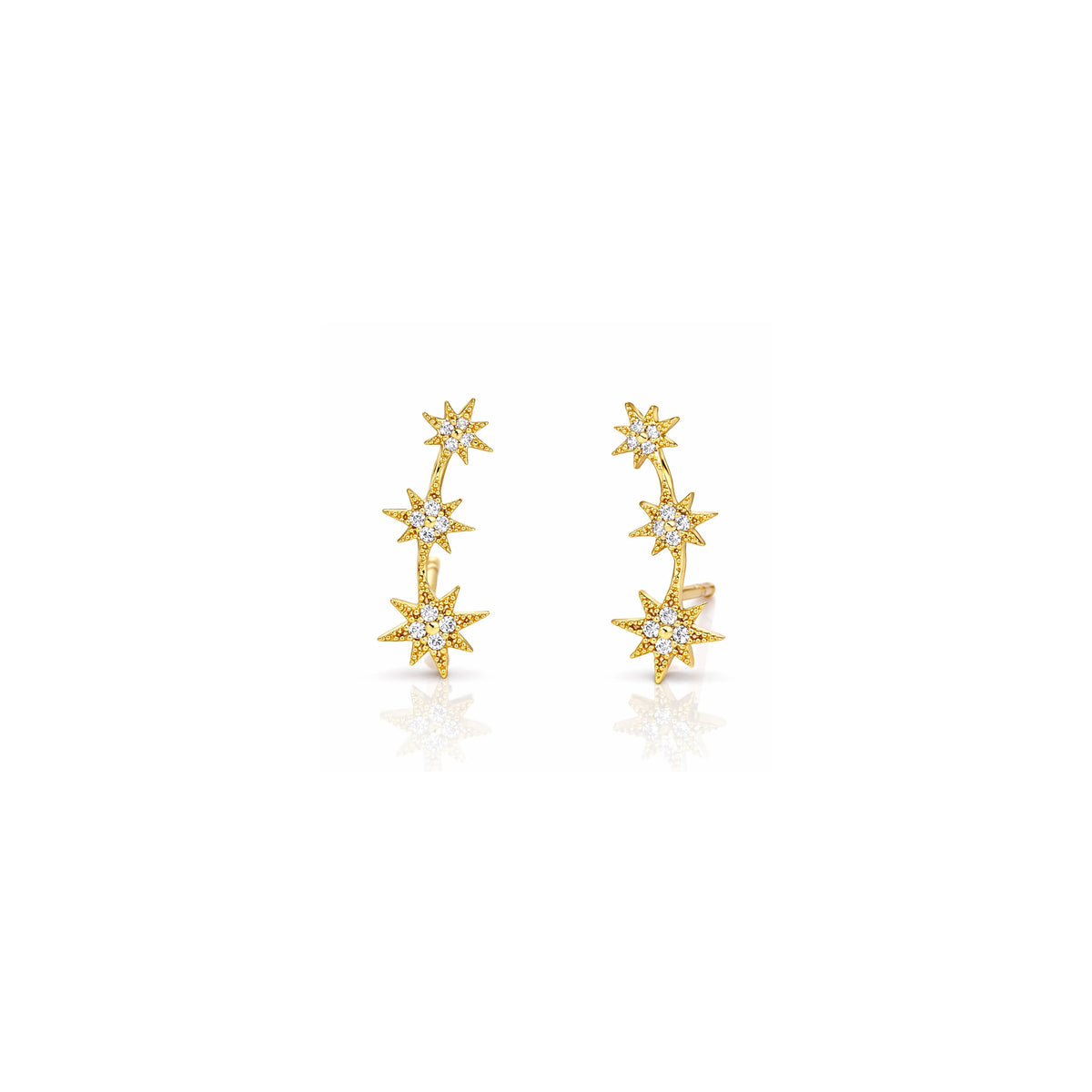 A pair of gold starburst earrings with small clear gemstones, displayed on a clean white background with a soft reflection below.