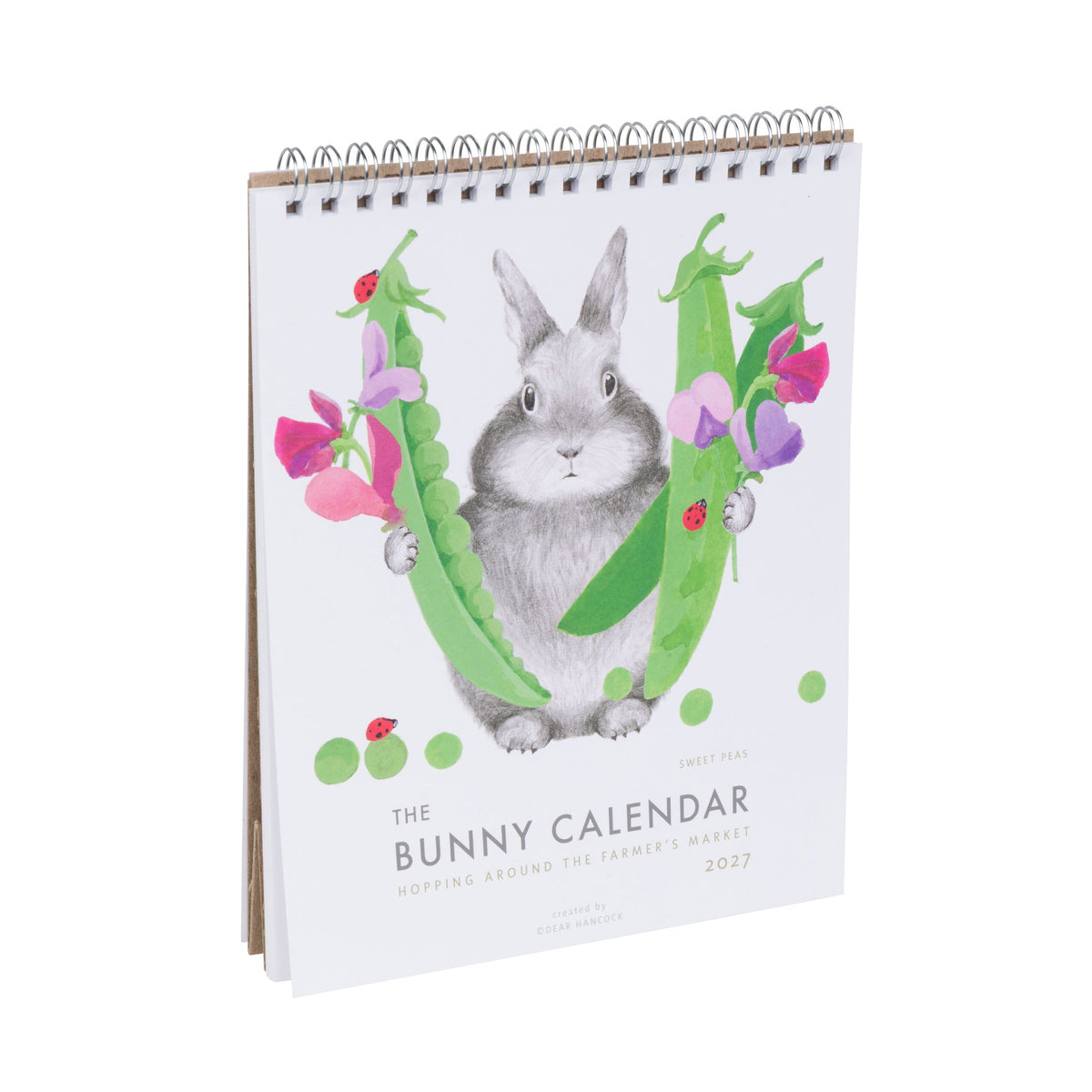 The Bunny Calendar 2027 featuring a watercolor illustration of a gray bunny surrounded by green peas and pink and purple flowers, on a white background with a gold spiral binding.
