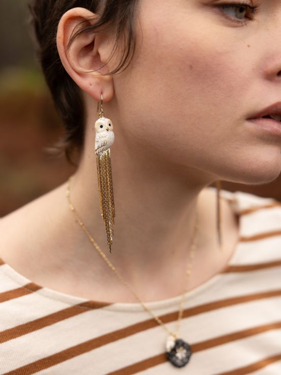 Make a statement in these shimmery white and gold owl earrings!    With cascading gold fringe, these dangly earrings feature hand-painted owls. Pair them with any outfit to level up your look and serve glamour owl realness.  Lead and Nickel-free Material: Porcelain, Gold-plated Brass Designed in Toulouse, France