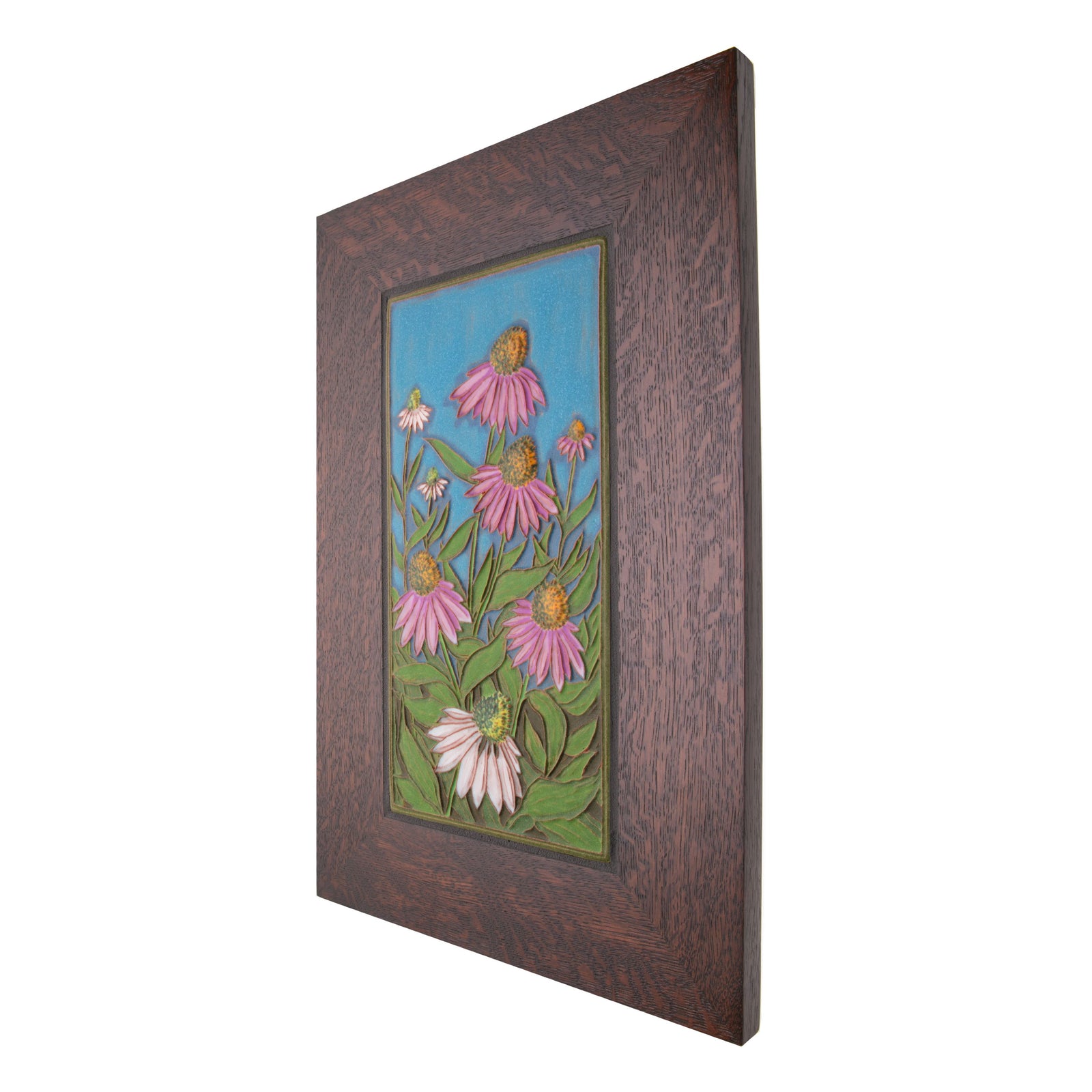 Expertly handcrafted in an artisan workshop in Canton, Ohio, this ceramic tile features a relief of purple and white cornflowers on a blue background. The tile is surrounded by a 2.5" quarter sawn oak frame.  Each tile is signed by the artist and has a notch in the wood frame.  Size including frame: 17" x 11"