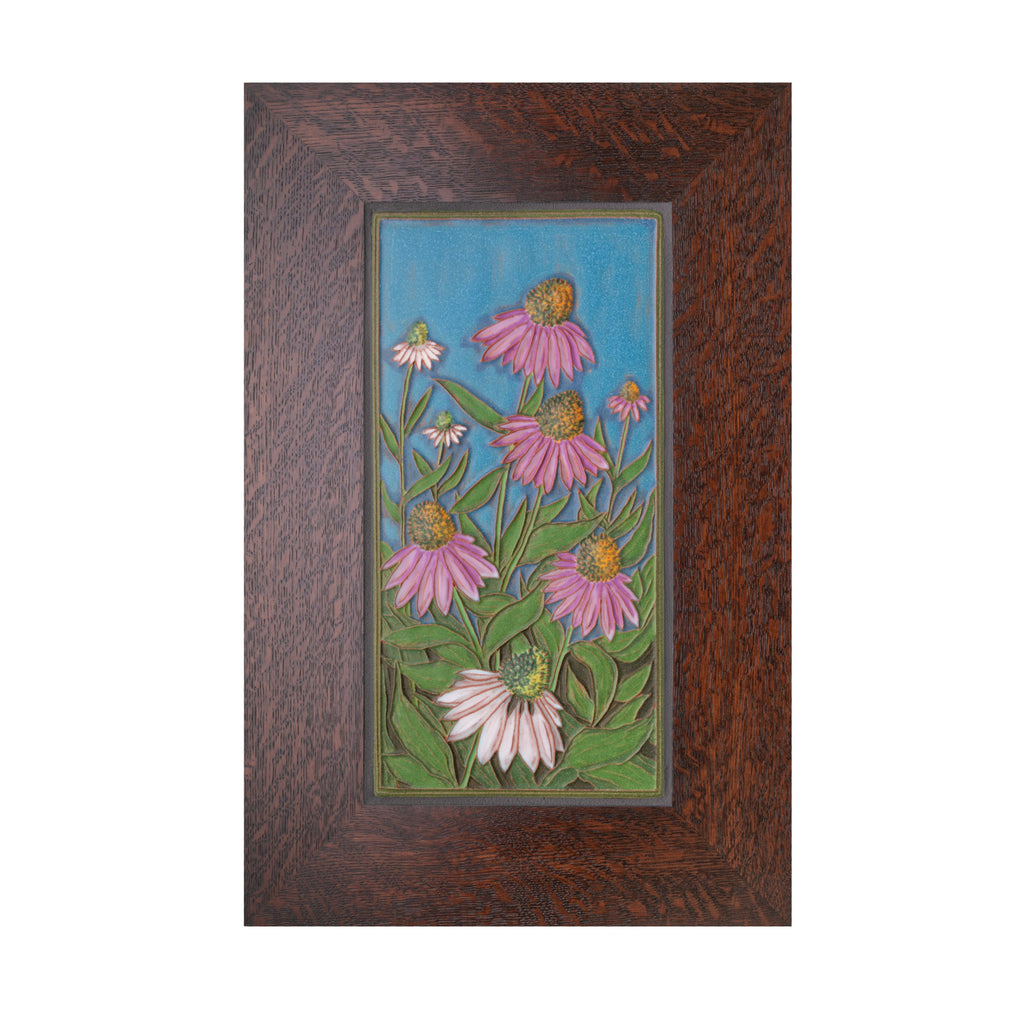 Expertly handcrafted in an artisan workshop in Canton, Ohio, this ceramic tile features a relief of purple and white cornflowers on a blue background. The tile is surrounded by a 2.5" quarter sawn oak frame.  Each tile is signed by the artist and has a notch in the wood frame.  Size including frame: 17" x 11"