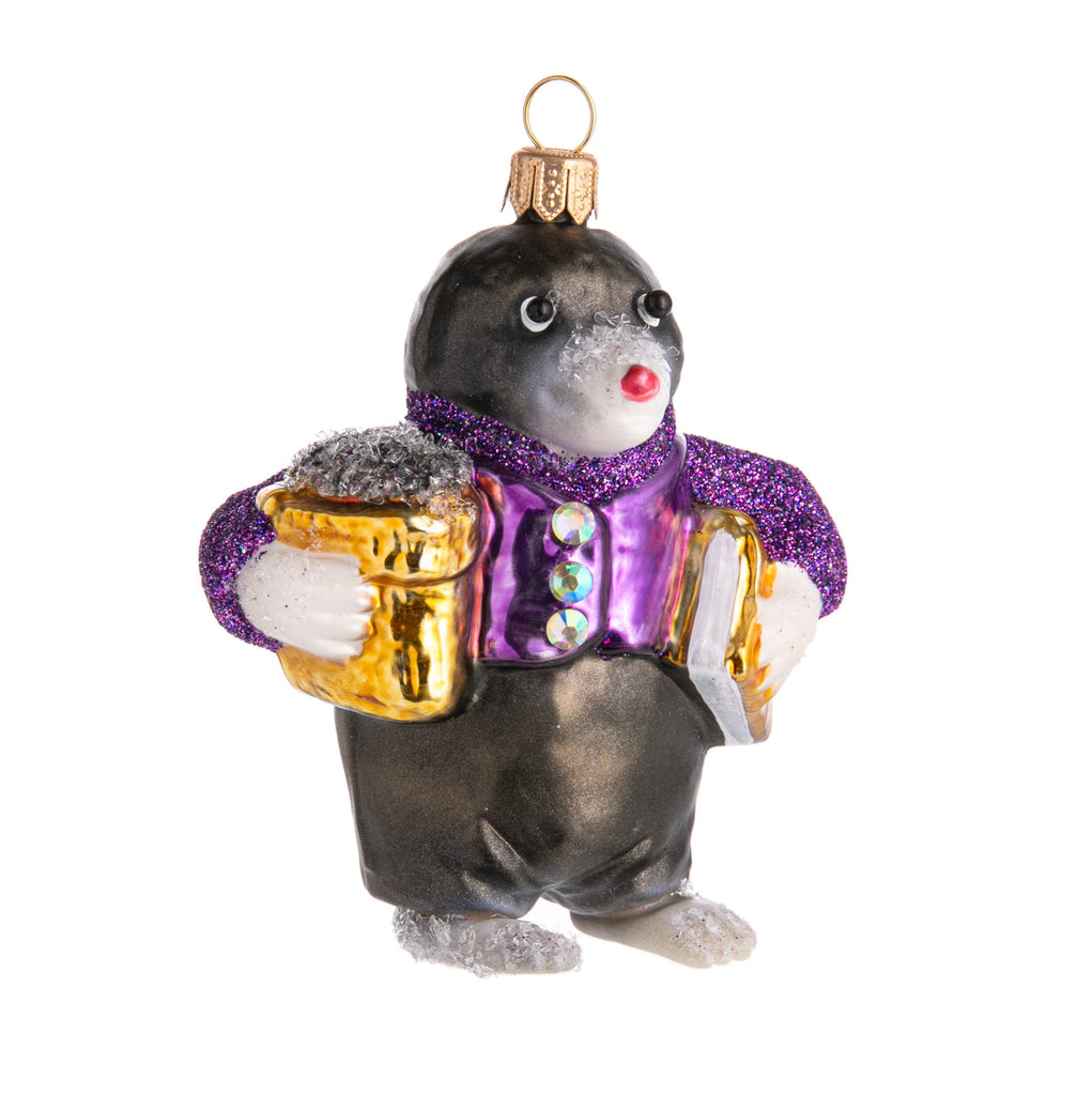 This little mole is ready to party! With his sparkly purple shirt with rhinestone buttons and arms loaded with gifts, he makes the cutest little guest to add to your festive decor. Hand finished, hand glittered glass ornament Dimensions: 3.5" x 3"