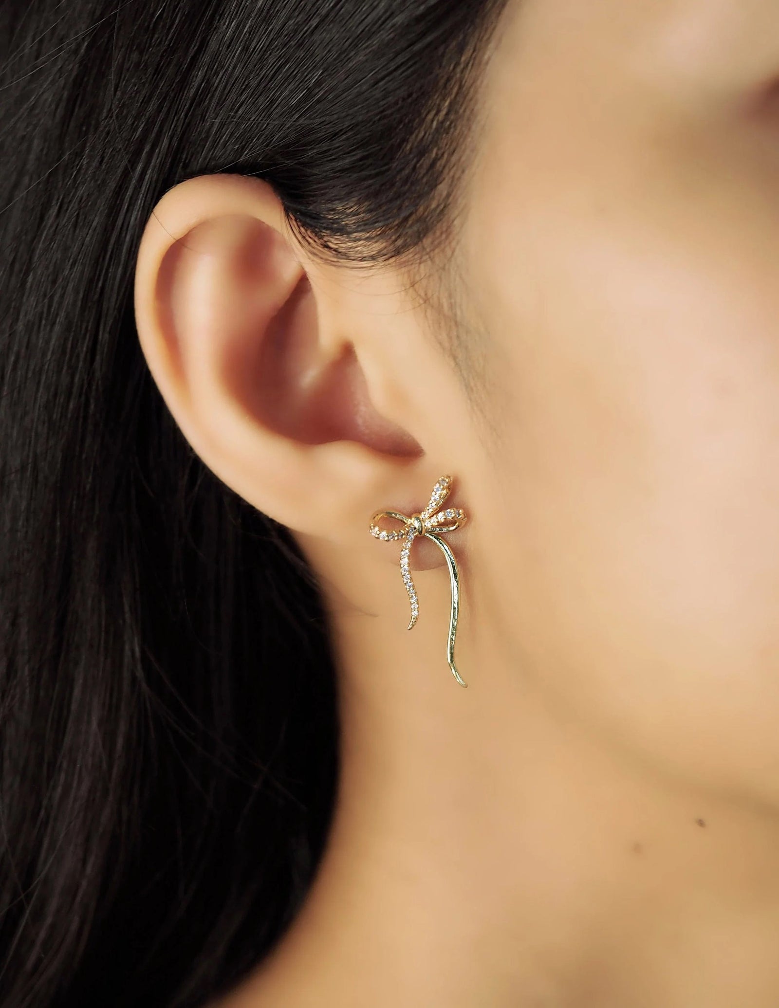 Adorn your ears with these dainty and delicate bows. With gold-plated brass detail and CZ sparkle, these stud post earrings will add subtle glam to any look. Perfect for a birthday gift to a loved one, or to yourself. Gold-plated Brass, CZ Stud post backing Dimensions: Approx. 0.75" Lead and Nickel-free