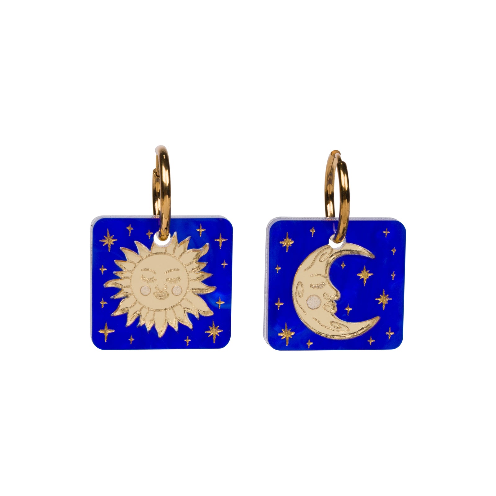 A pair of square cobalt blue glass earrings with gold-toned metal hoops featuring a sun face on one charm and a crescent moon with stars on the other, set against a plain white background.