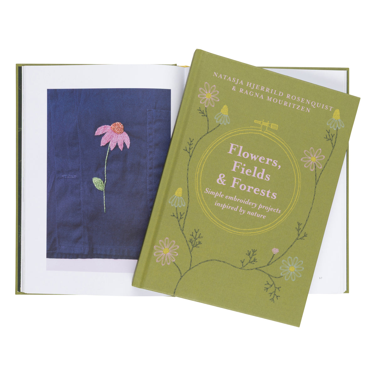 An open embroidery book with a green cover titled "Flowers, Fields & Forests" placed over an open page showing a navy blue fabric sample with a pink flower embroidery.