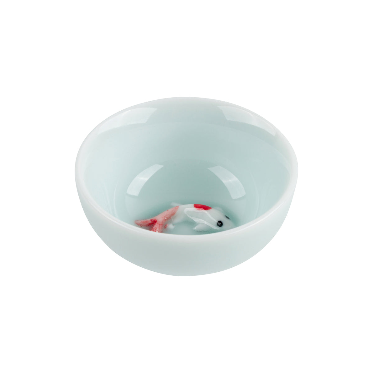 A glossy pale aqua ceramic bowl with a small white and red fish figurine inside, photographed on a clean white background.