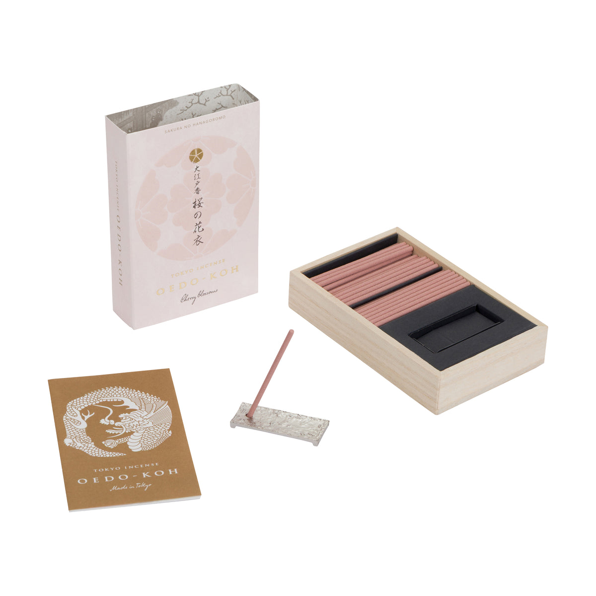 A set of Oido-Koh incense sticks shown with its light pink packaging box, a wooden tray holding the incense sticks, a brown card insert, and a single incense stick resting on a small square dish, all arranged on a clean white background.