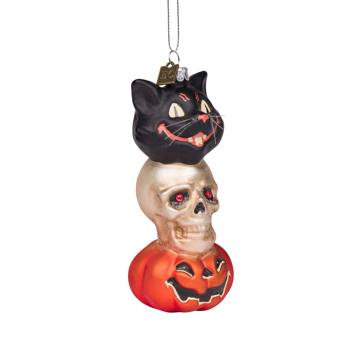 A stacked Halloween ornament featuring a black cat sitting on a metallic gold skull, which is in turn on an orange jack-o'-lantern pumpkin, hanging from a silver string against a plain white background.