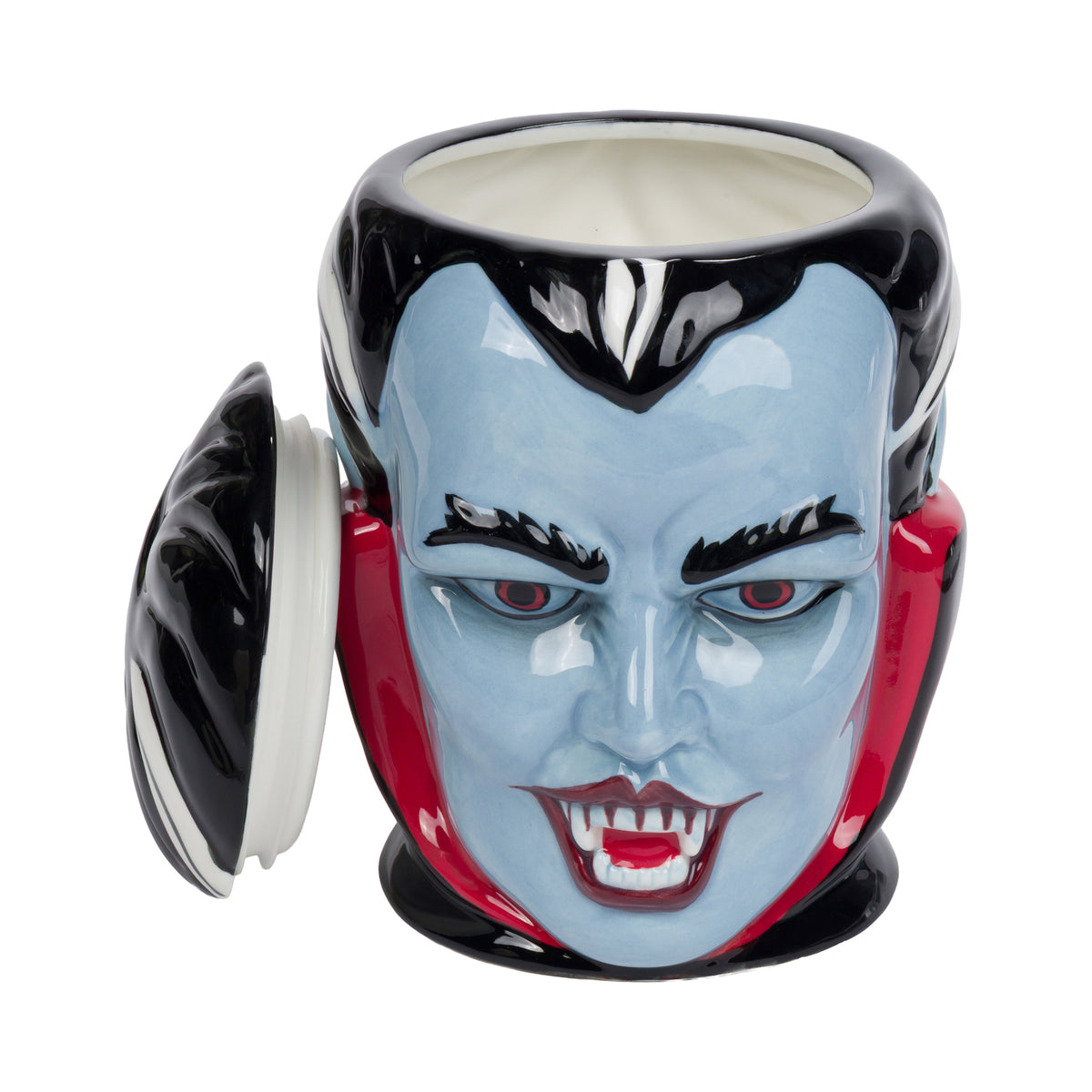 A ceramic vampire face cookie jar with its lid leaning against the left side. The mug features a glossy light blue face, black hair, red collar accents, and red vampire fangs, set against a plain white background.