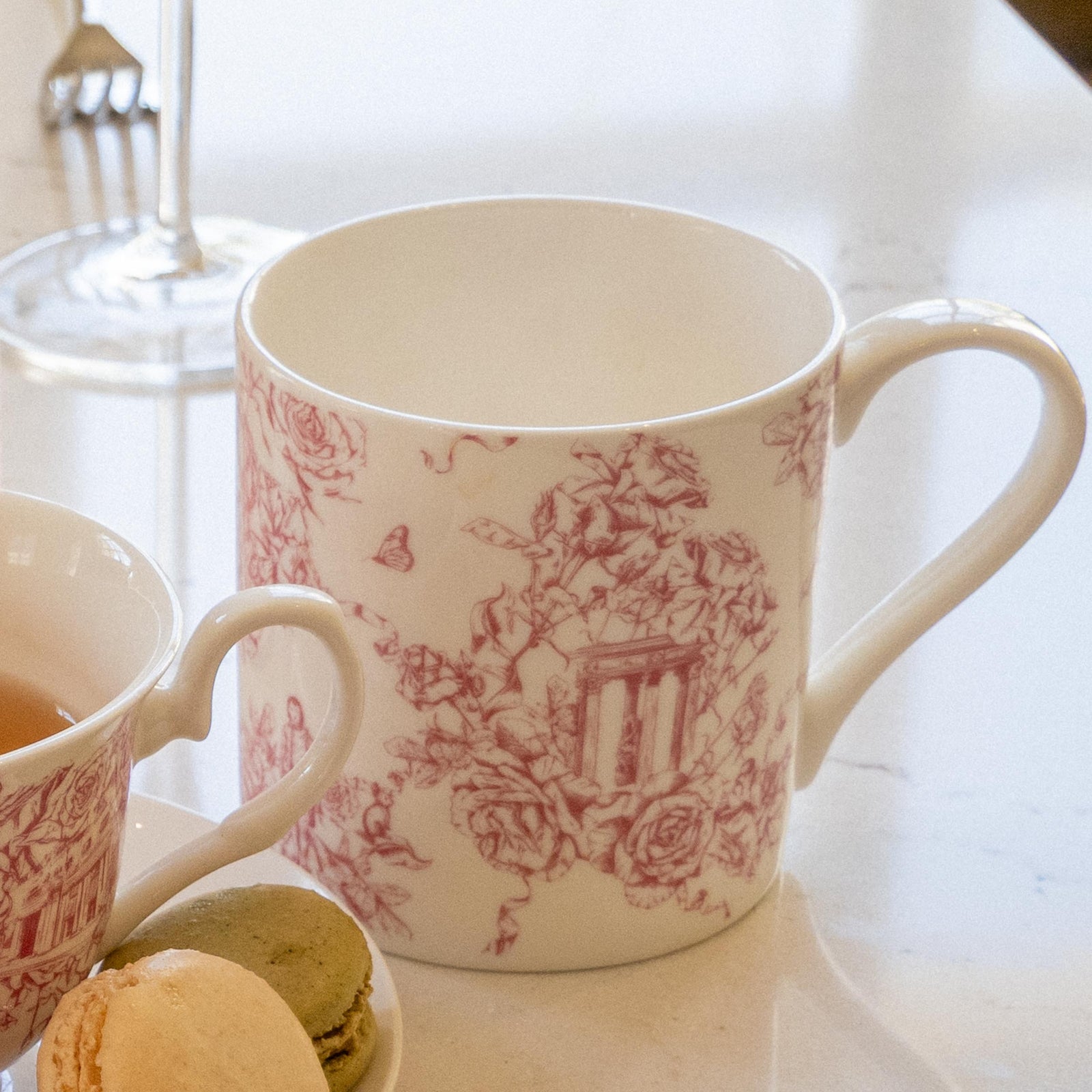 A white bone China mug with a red 'Rose Garden toile' print featuring floral patterns and architectural elements.