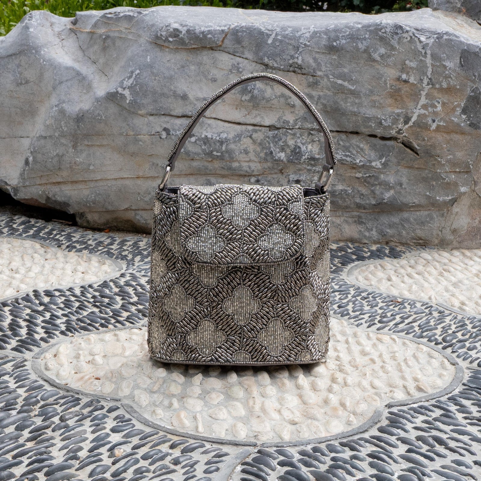 A handbag with a geometric pebble tile pattern, featuring a beaded design in black and white, with a satin and vegan leather lining, and a magnetic snap fastening.