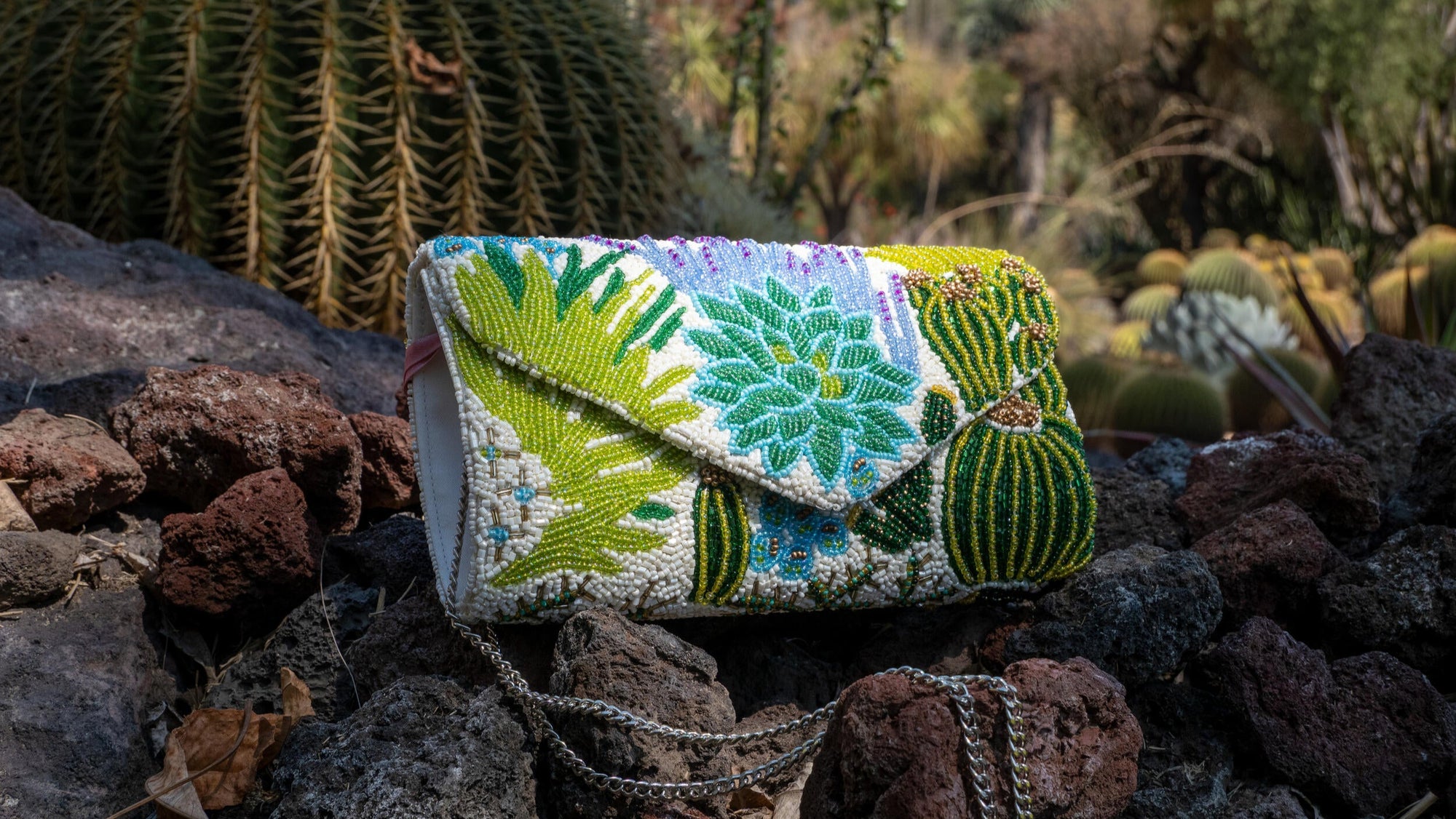 Decorative clutch bag with floral patterns on a rocky surface with cacti in the background