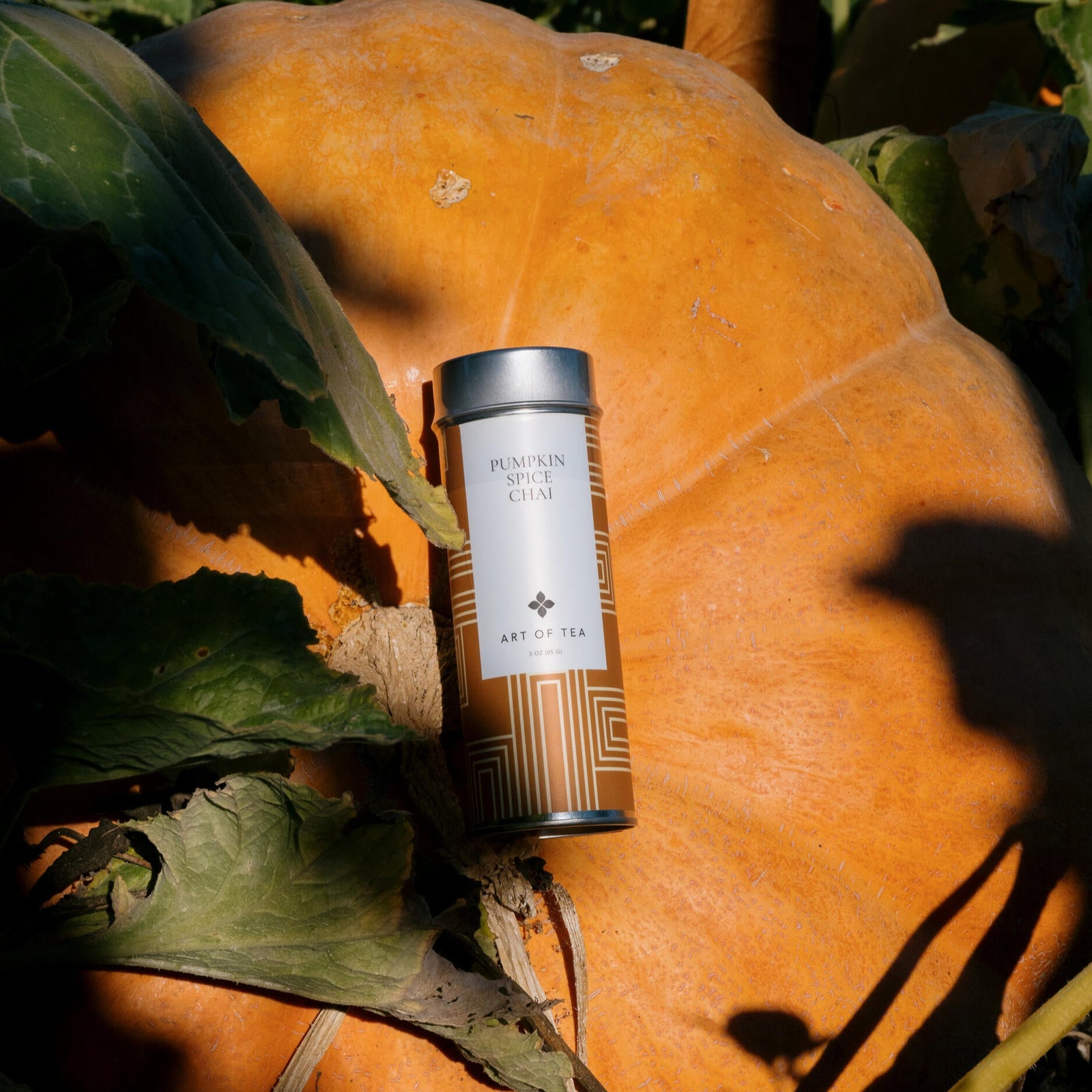 A decorative metal canister of Art of Tea branded Pumpkin Spice Chai loose leaf tea, with a beige and orange geometric design on the label.