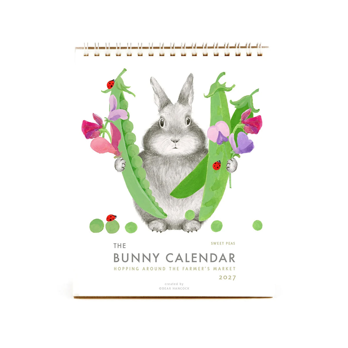The Bunny Calendar 2027 featuring a watercolor illustration of a gray bunny surrounded by green peas and pink and purple flowers, on a white background with a gold spiral binding.