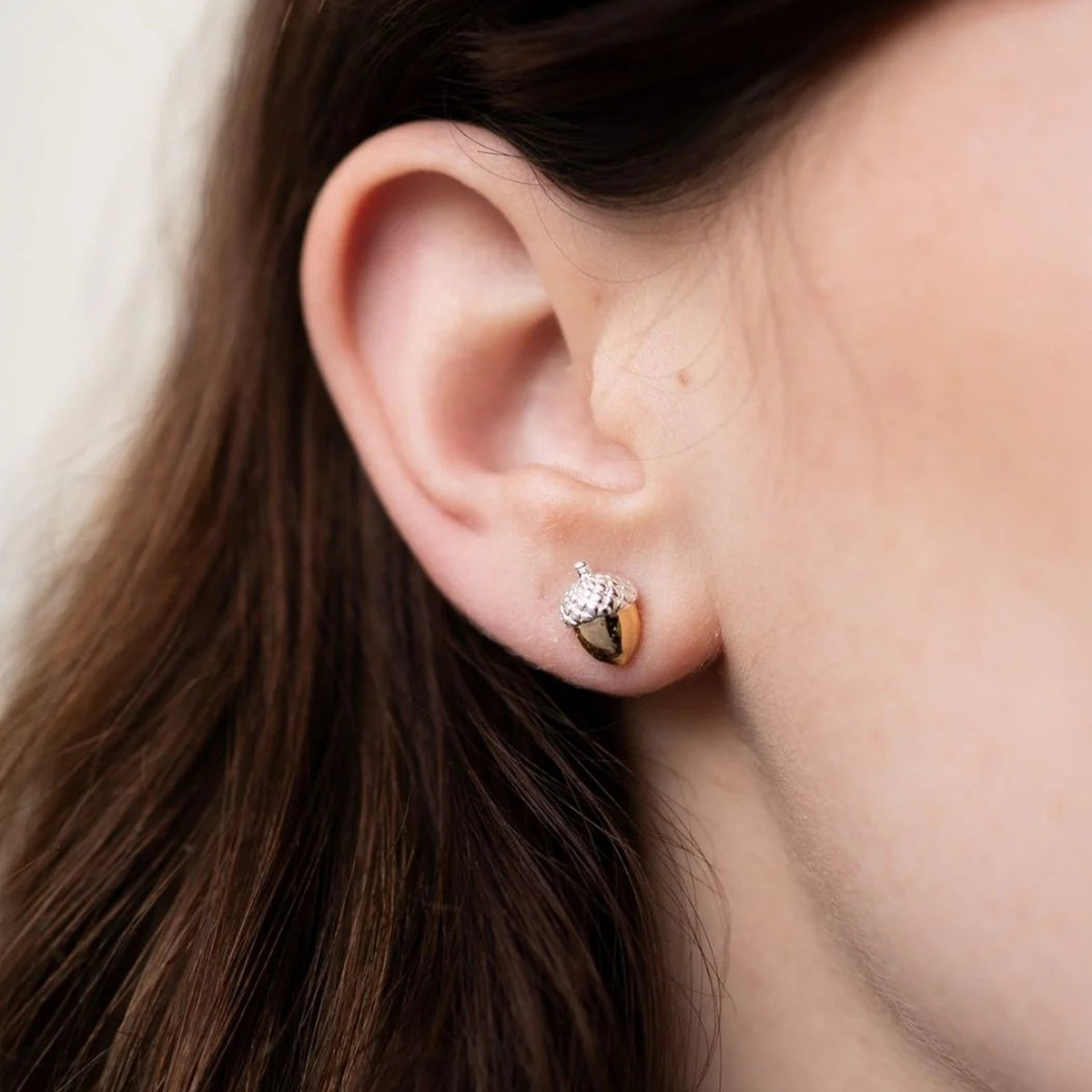 Close-up of an ear wearing a stud earring shaped like a small acorn.