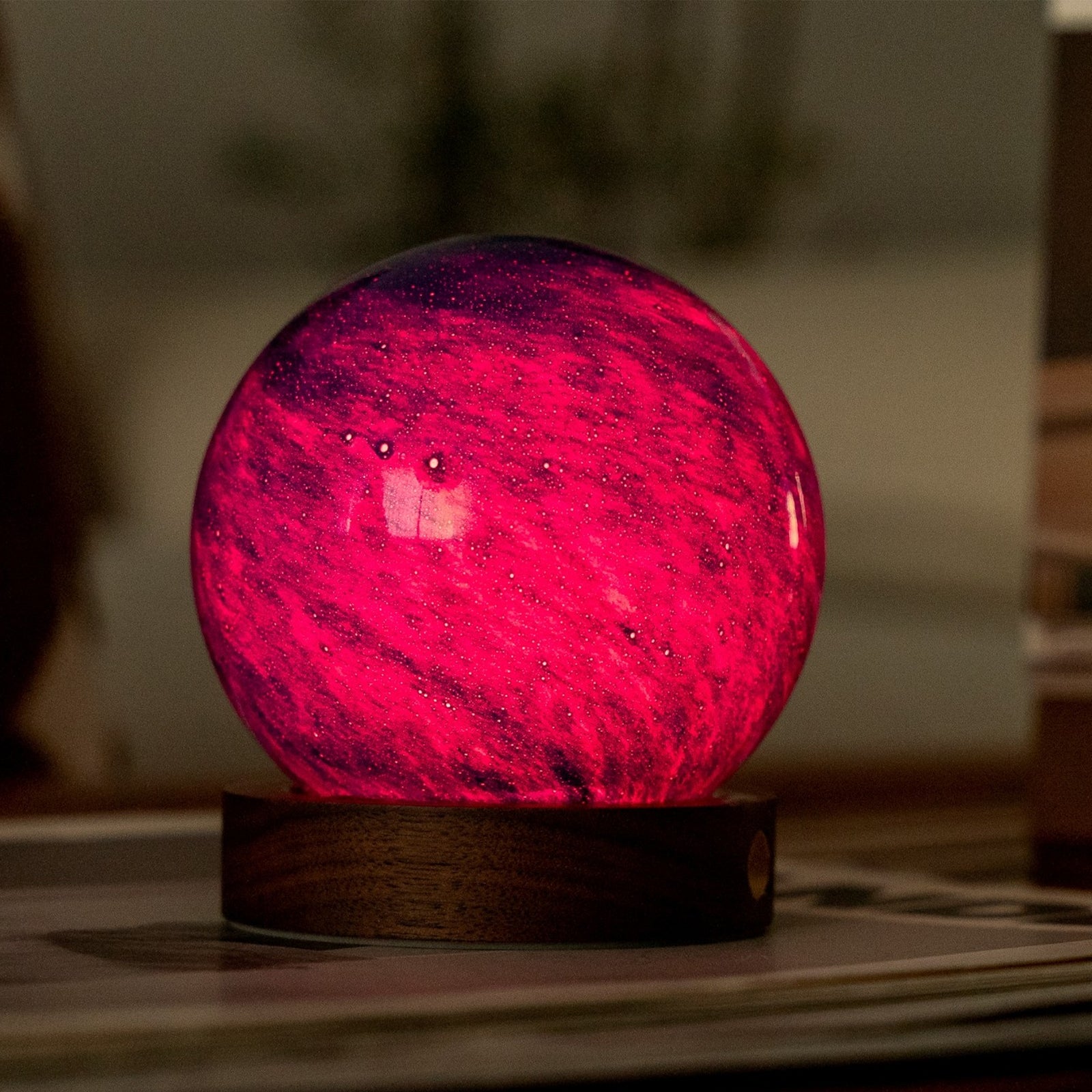 A glowing crystal ball night light with a purple and blue marbled pattern, resting on a dark wooden base with a small gold button, isolated on a white background.