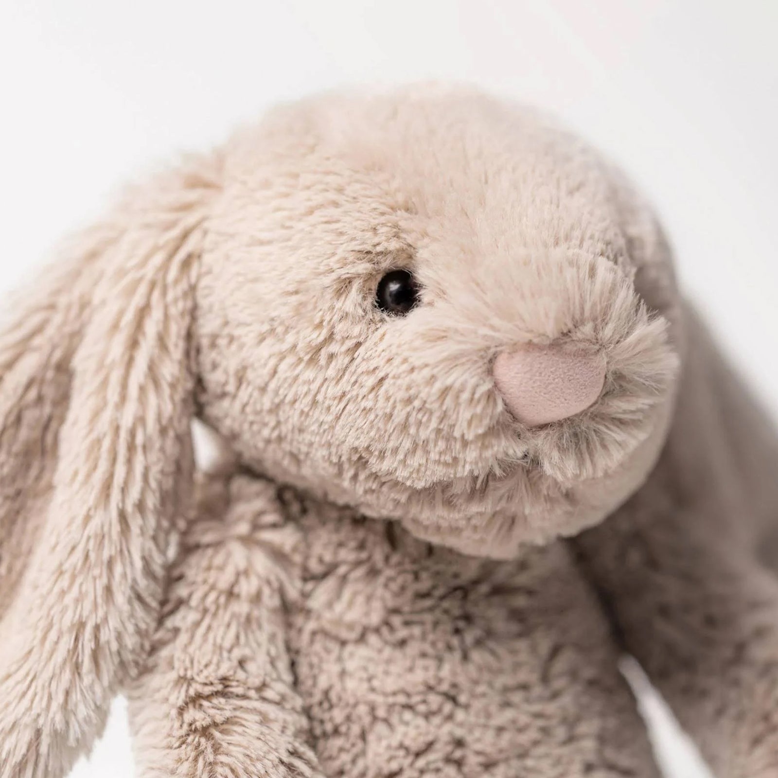 A plush stuffed Jellycat Bashful Bunny toy in a light taupe-beige color, sitting upright against a seamless white background.