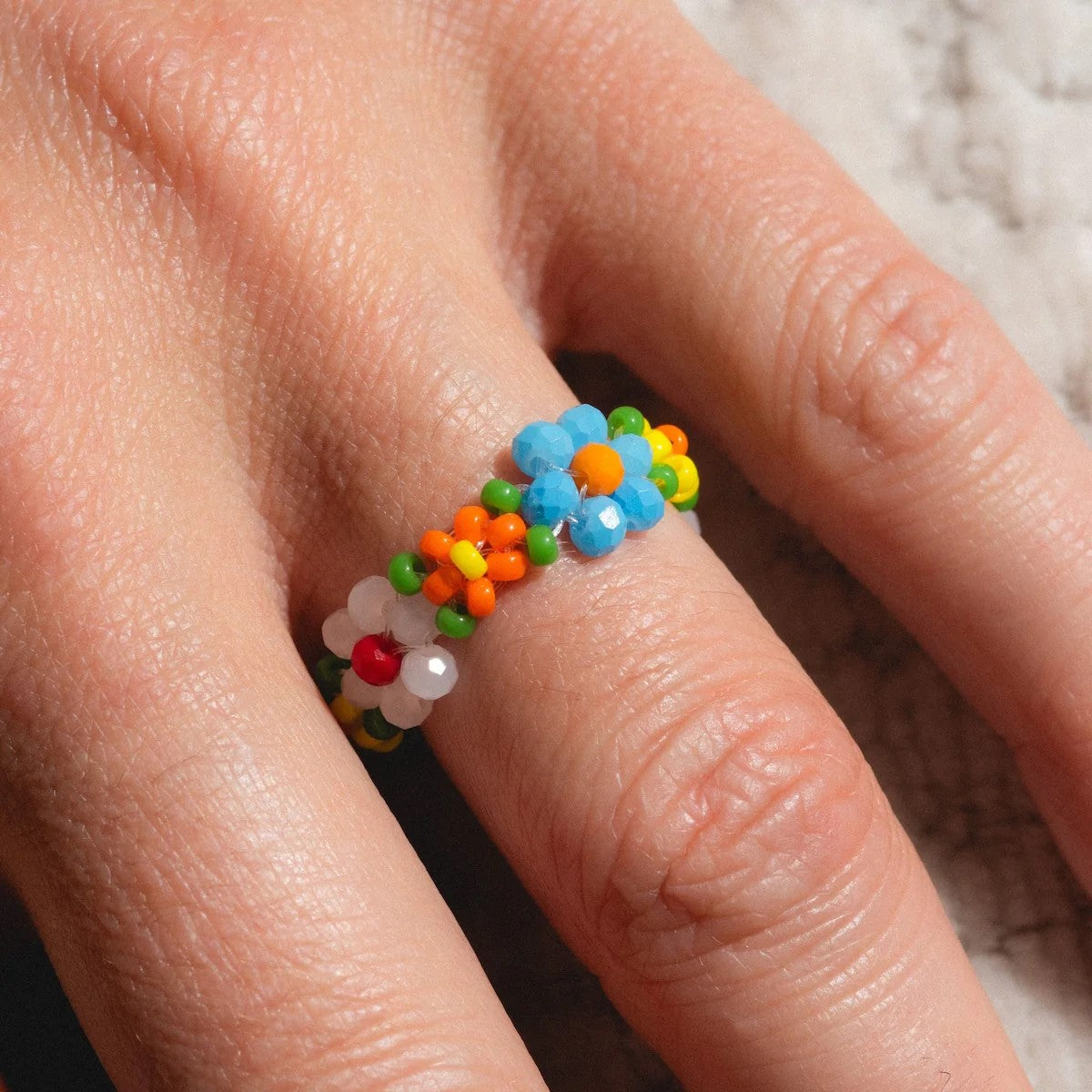 Colorful beaded daisy chain ring on a white background