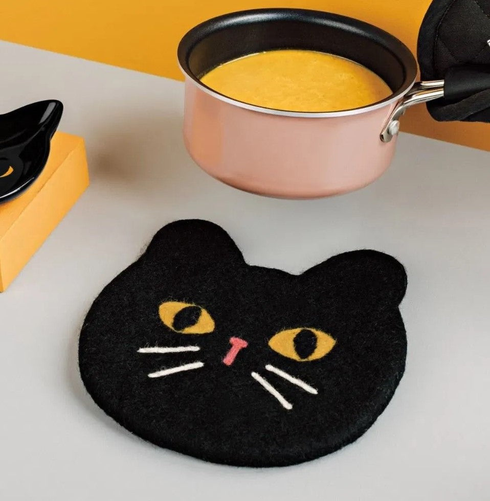 Black cat-shaped trivet with yellow eyes and a pink nose on a white background