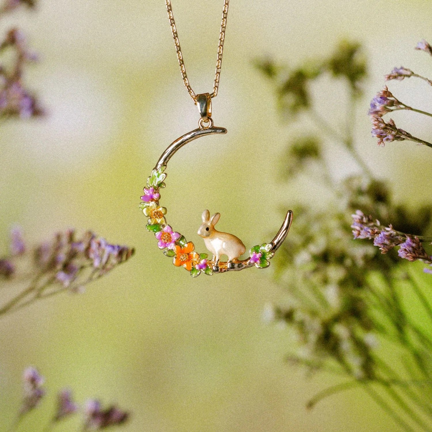 Gold necklace with a crescent moon pendant featuring a bunny and flowers on a white background