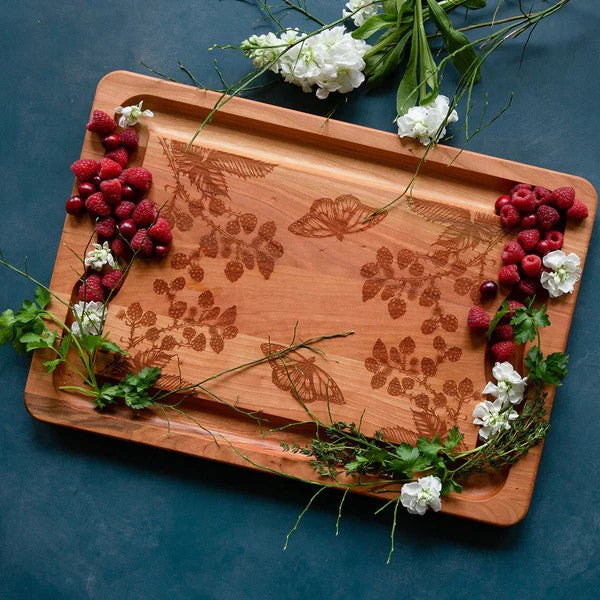 Wooden cutting board with engraved floral and butterfly designs on a white background
