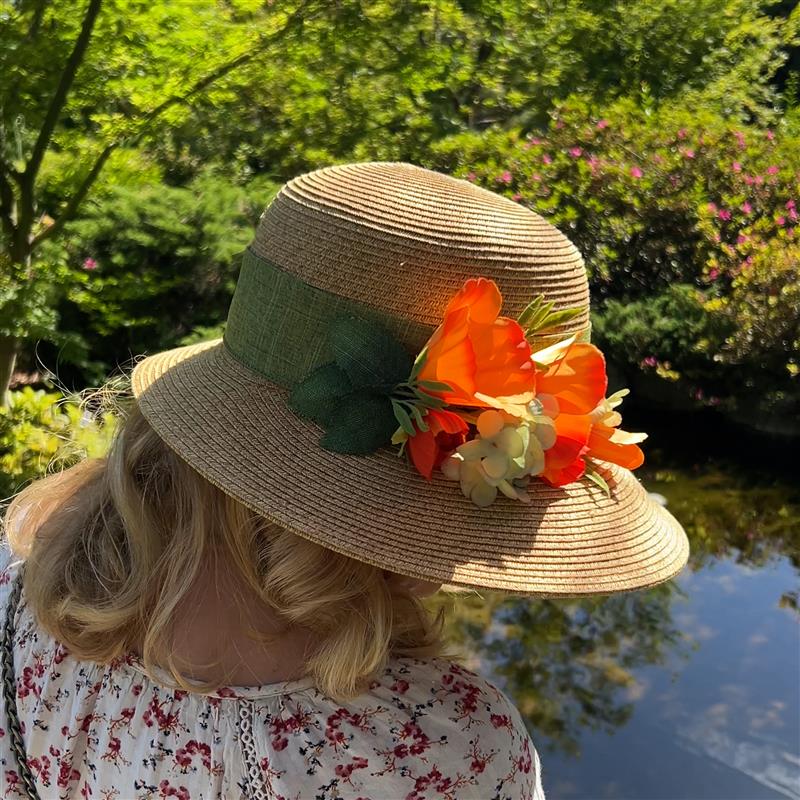 Person wearing a straw hat with floral decorations in a garden setting