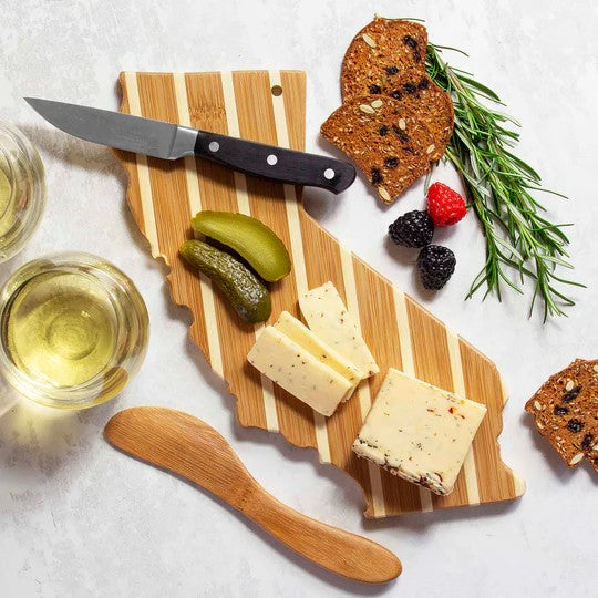 Wooden cutting board with cheese, crackers, and pickles on a light surface.