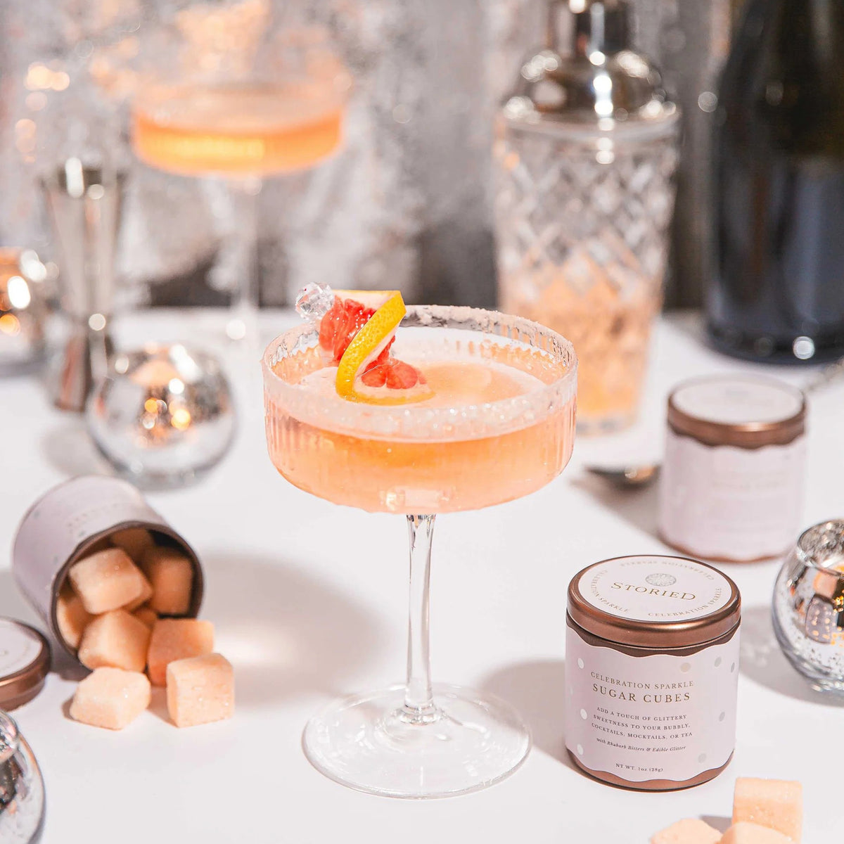 Cocktail in a glass with a garnish on a table with a jar of sugar cubes and blurred background.