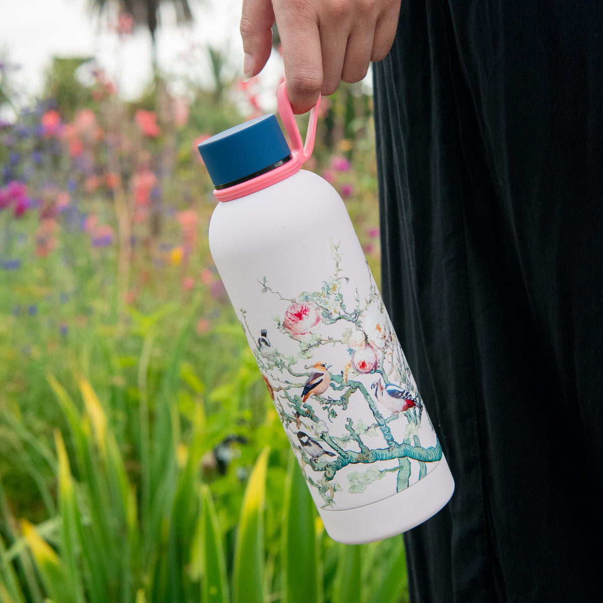 Person holding a water bottle with floral design in a garden setting