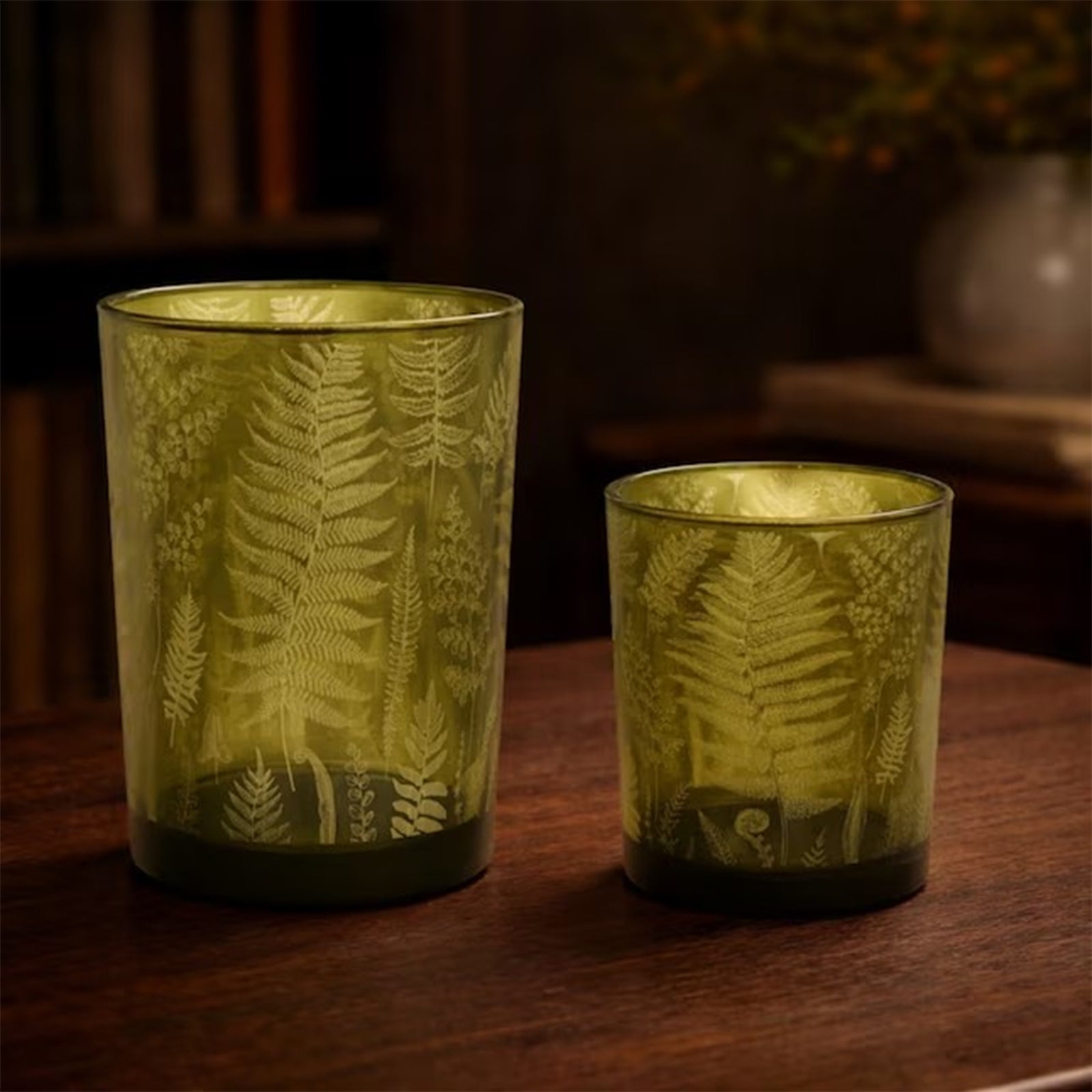 Two glass votive candle holders in green glass, decorated with a fern-leaf pattern, on a white background.