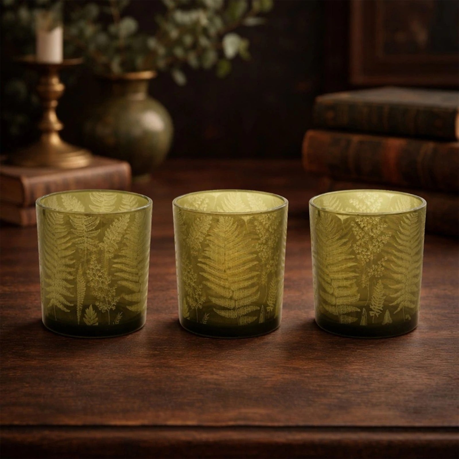 Green glass candle holder votive, decorated with a fern leaf print, on a white background