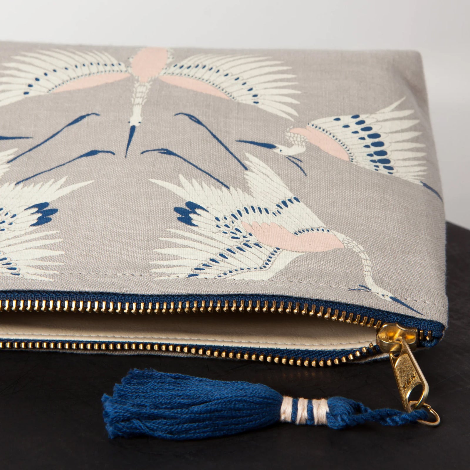 A timeless print of birds in motion. Worldly and full of grace, this aerial assembly of Cranes is elevated by the intricate linework on this design. Printed onto a vintage style grey linen base and finished off with a metallic gold zipper and midnight blue tassel. 9 x 5 inches. 100% Linen with Vegan Leather Lining. 