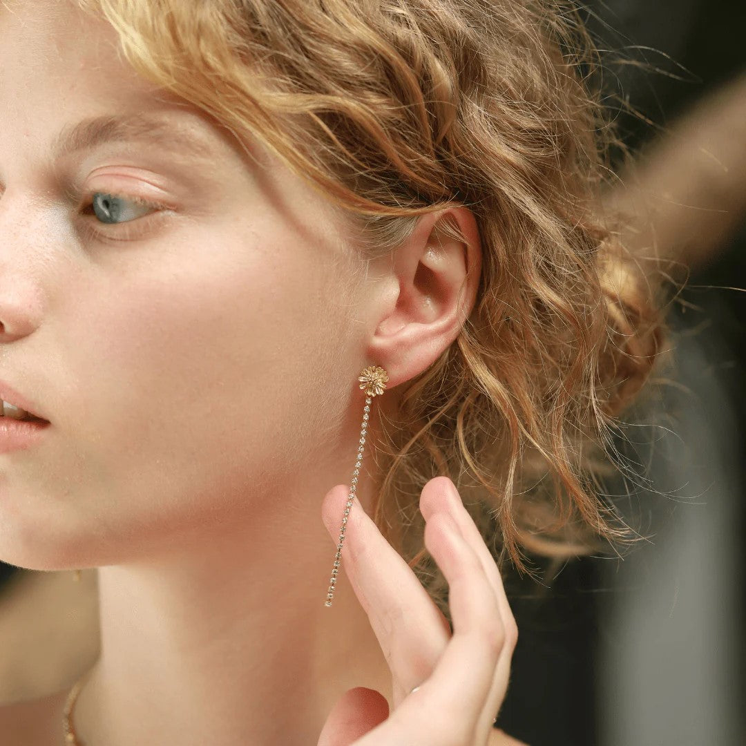 Make your presence known with these dazzling flower studs! Featuring a center gold plated flower stud with a cascade of tiny crystals, these pretty earrings are both effortlessly elegant and stunningly striking. Gold-Plated Brass with crystal accents. Dimensions: 0.25" W x 3" L.