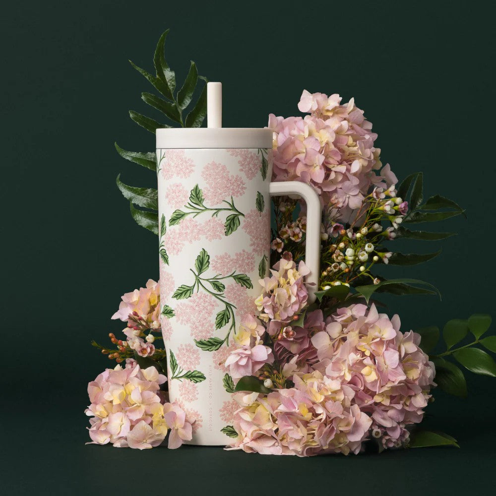 Floral-patterned tumbler surrounded by pink flowers on a dark background