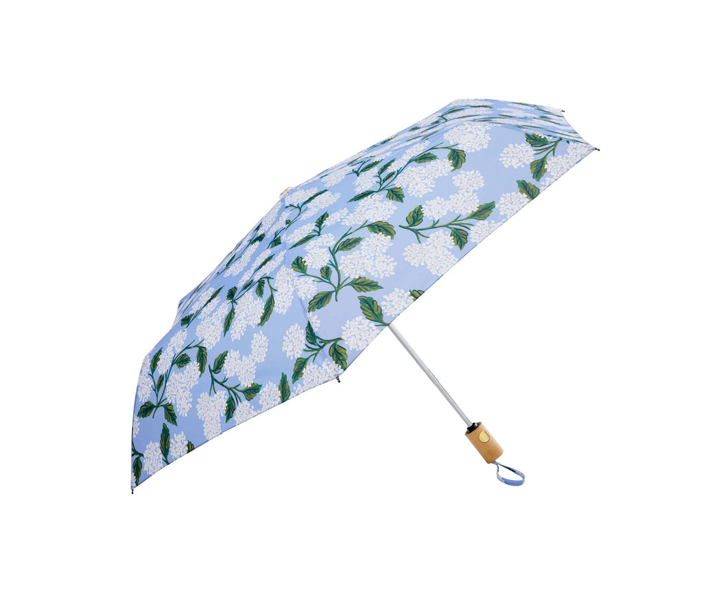 Add blue skies and beautiful blooms to all rainy days with this cute and compact hydrangea print umbrella. It features a wooden handle, a patterned sleeve, and an auto open/close function. Dimensions: 43" open diameter, 11⅛" closed length. Wooden handle. Folds up to a portable size. Matching storage sleeve.
