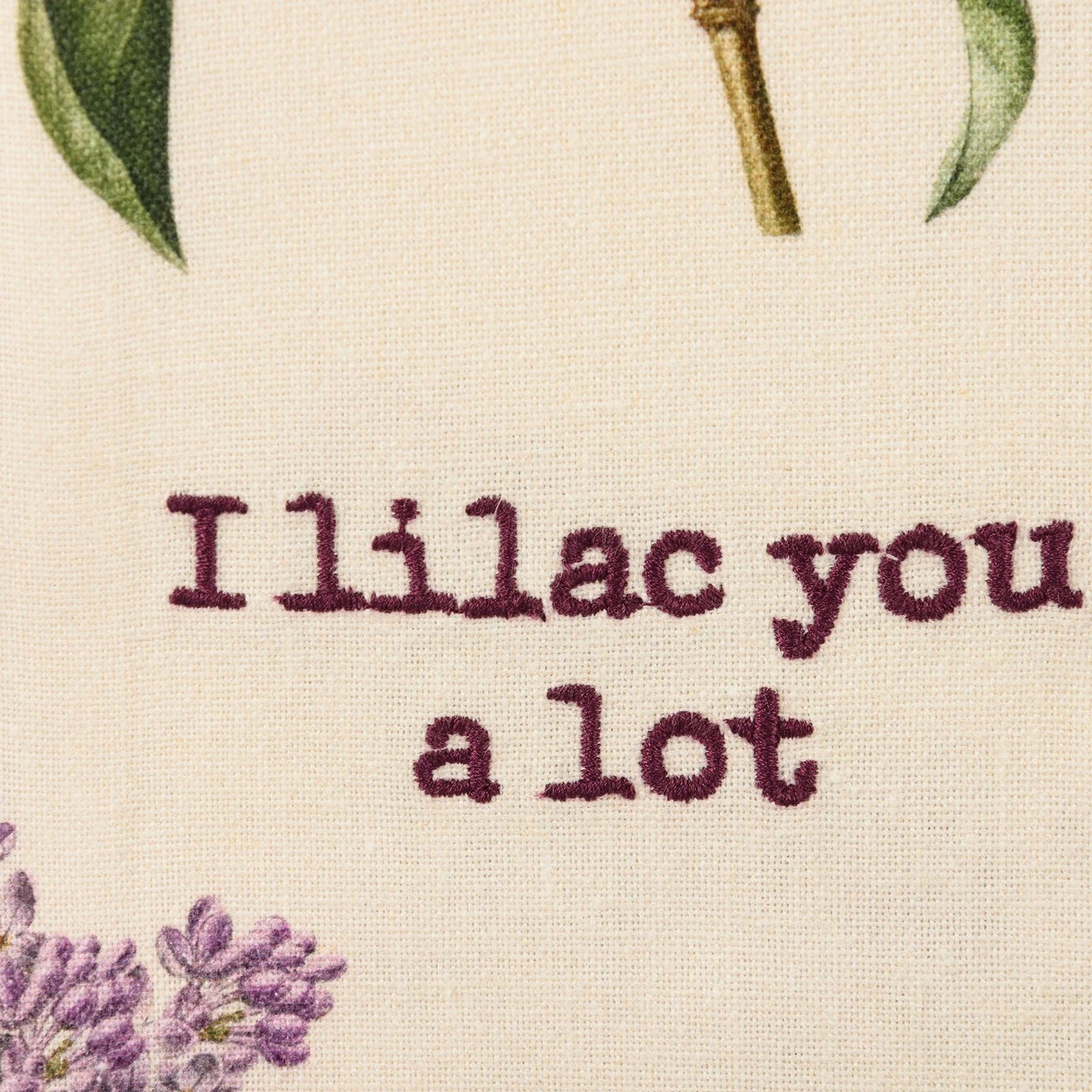 Beige towel with purple lilac flowers and text 'I lilac you a lot' on a white background