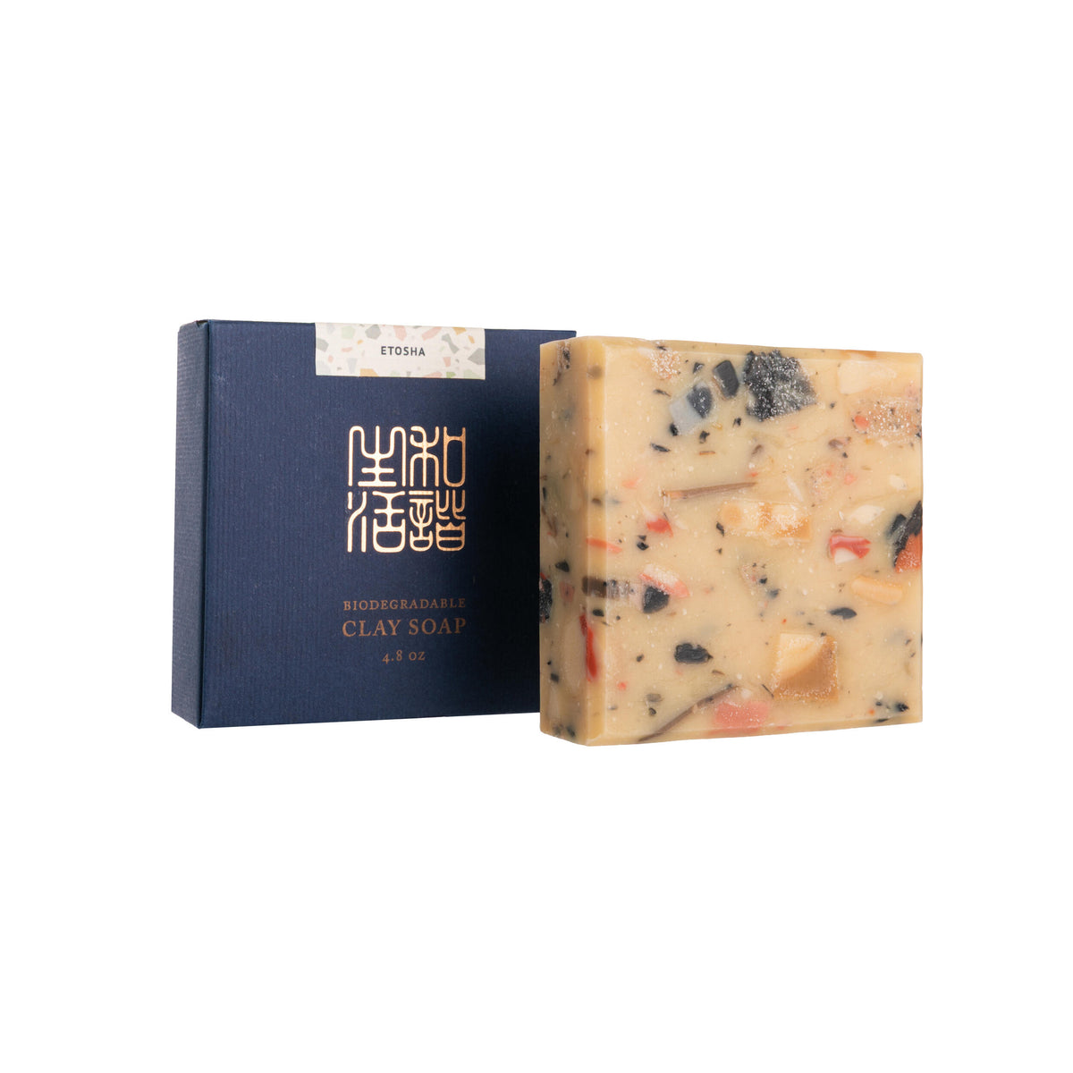 Bar of soap with visible ingredients next to a dark blue packaging box on a white background