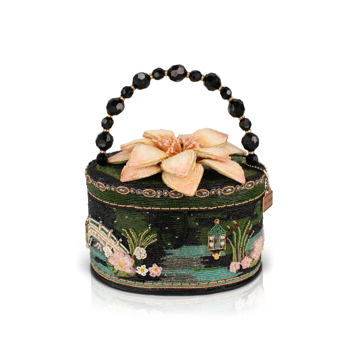 A small round handbag with a beaded black handle, featuring a dark green embroidered landscape design with a pink flower on top, set against a plain white background.
