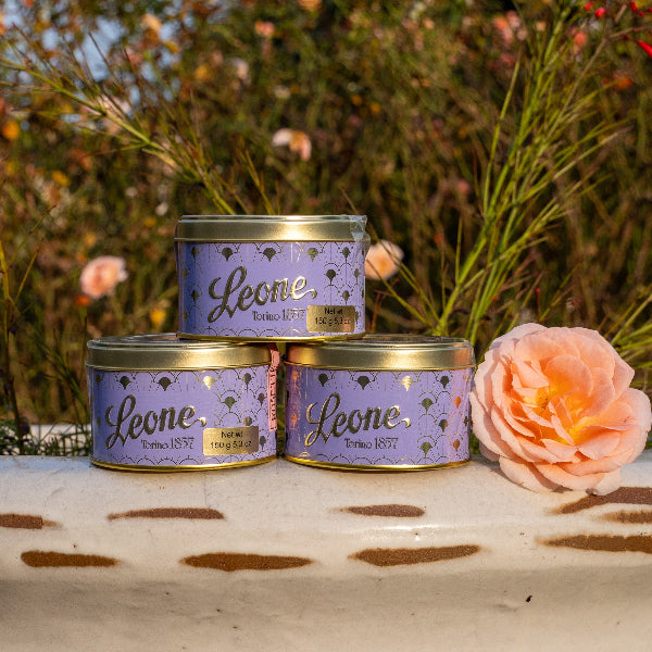 Three Leone tins stacked with a pink flower on a wooden surface outdoors.
