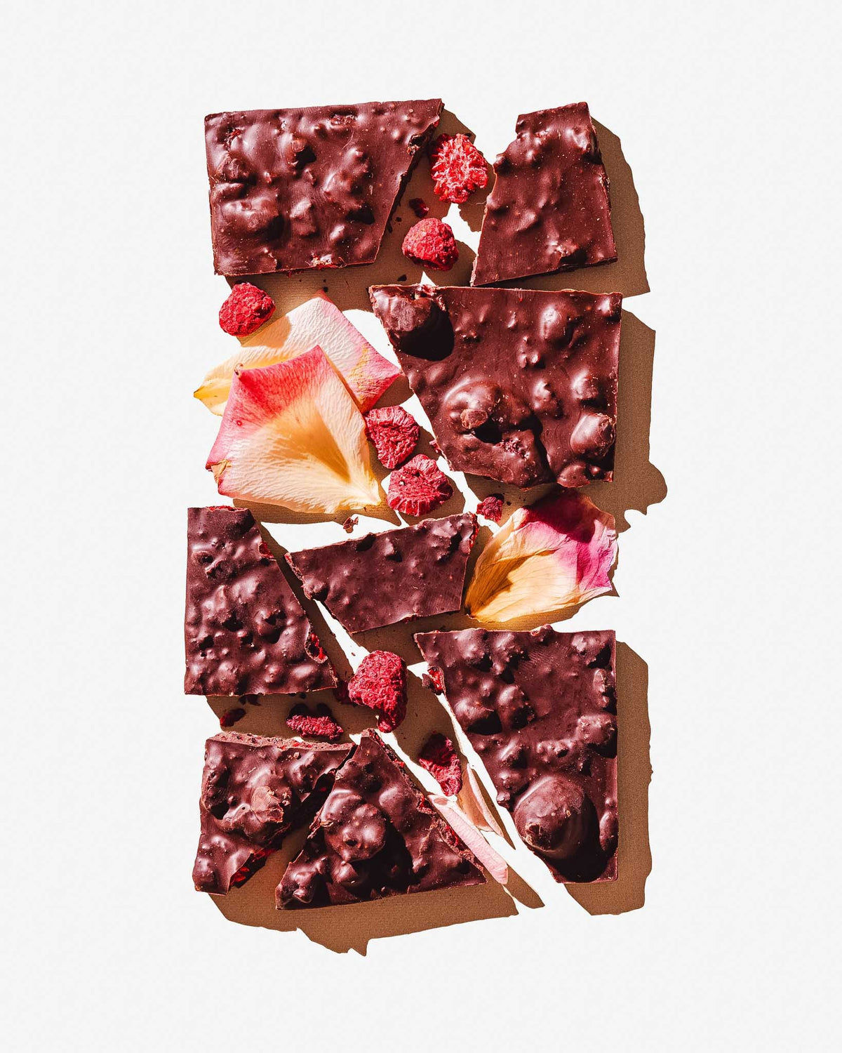 Chocolate bark with raspberries and rose petals on a white background