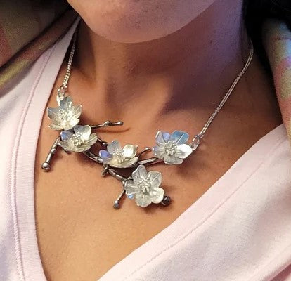 Indulge in the dramatic beauty inspired by Hokusai’s small blossoms with this handcrafted sterling silver cherry blossom branch necklace. Meticulously shaped and textured, it captures the essence of cherry blossoms on a branch, offering a dramatic and unique piece of wearable art. Material: Sterling silver Dimensions: Branch/blossoms: 4" x 1.5". Chain length 15"