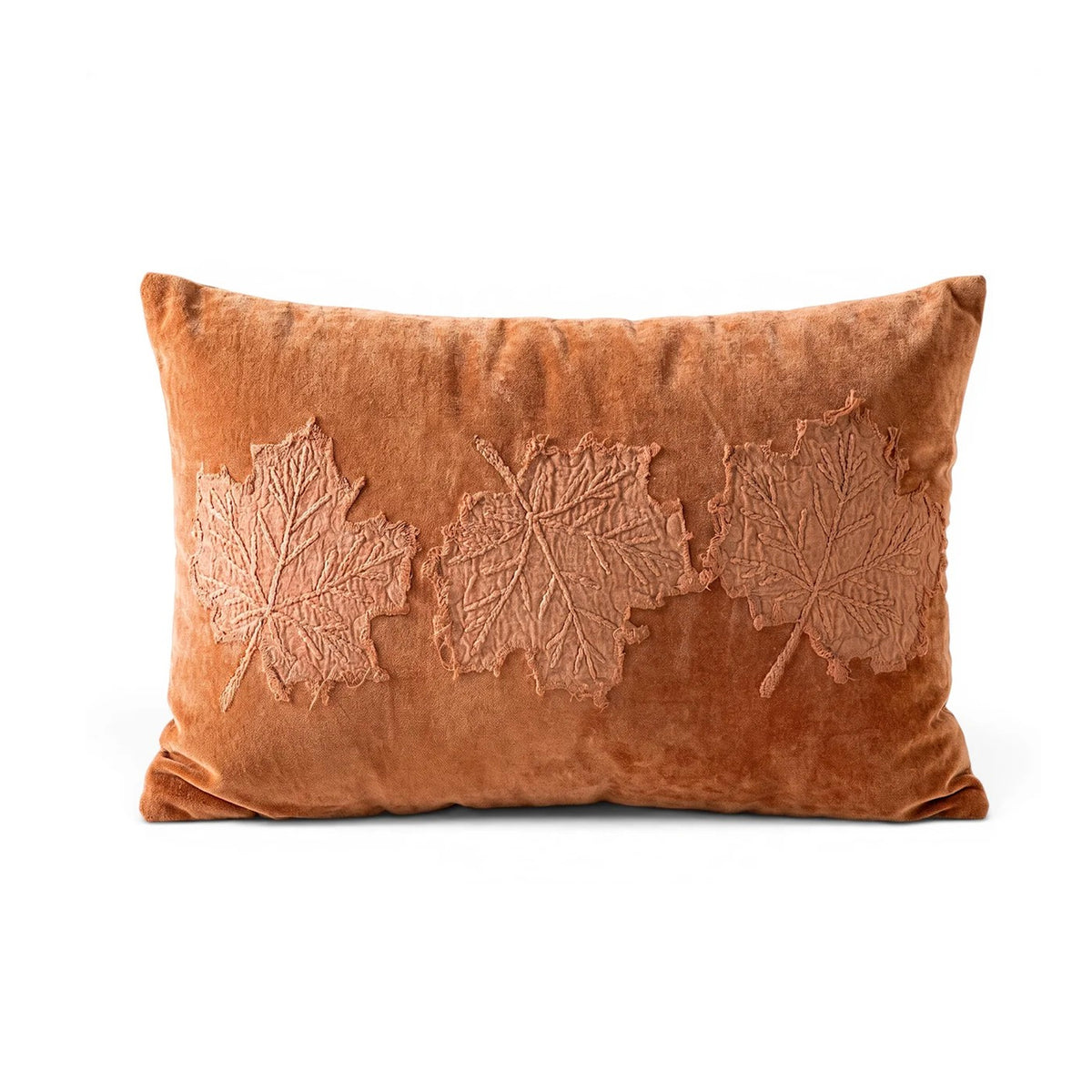 A rectangular rust-orange velvet throw pillow featuring three large, raised embossed maple leaf designs across the front, set against a plain white background.