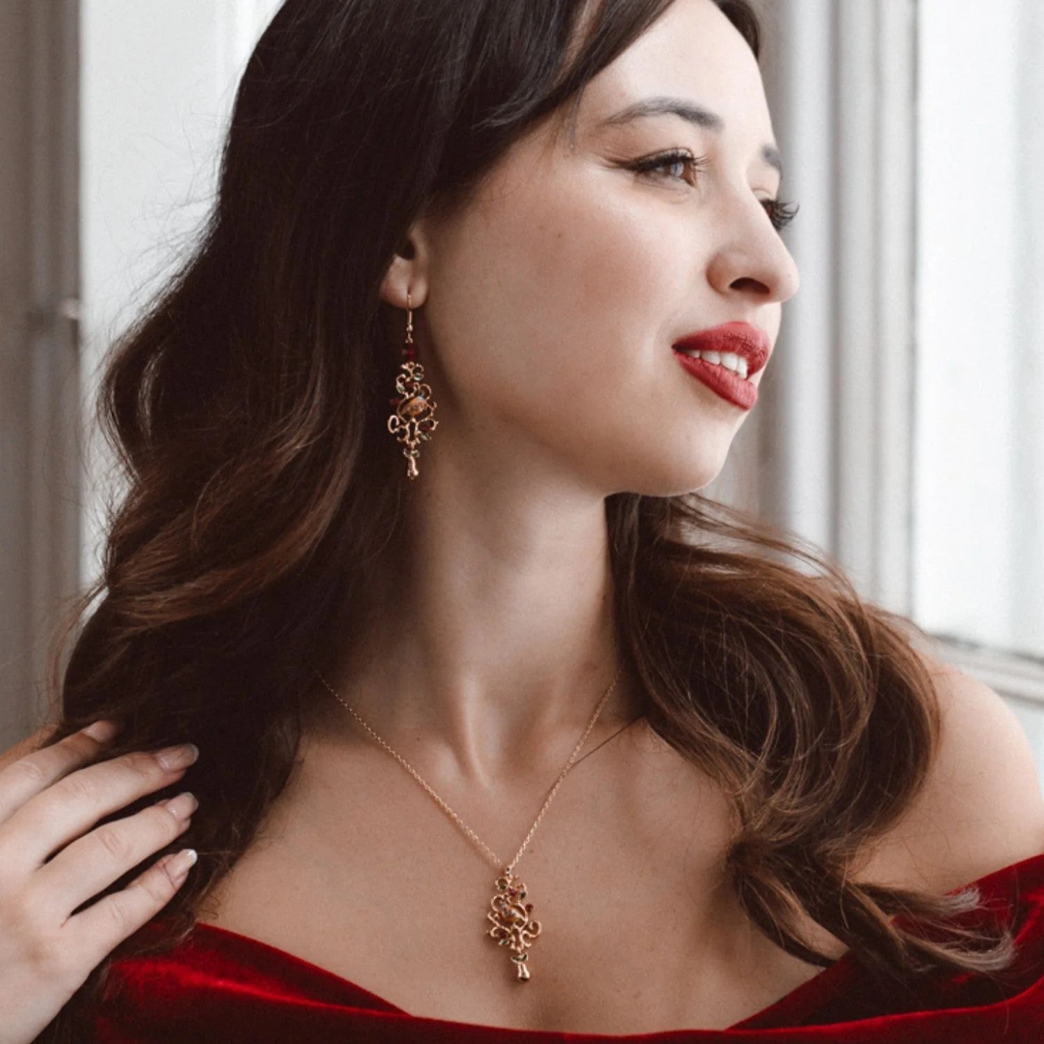 Dangle earrings featuring a partridge in a pear tree on a gold filigree base, on a white background.