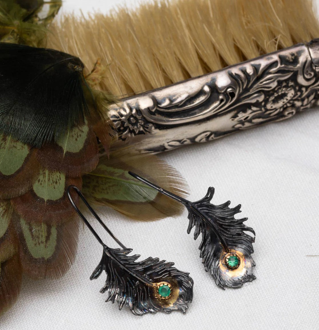 Feather-shaped earrings with green gemstones on a white background